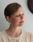 Woman wearing drop herkimer earrings standing next to a flower painting