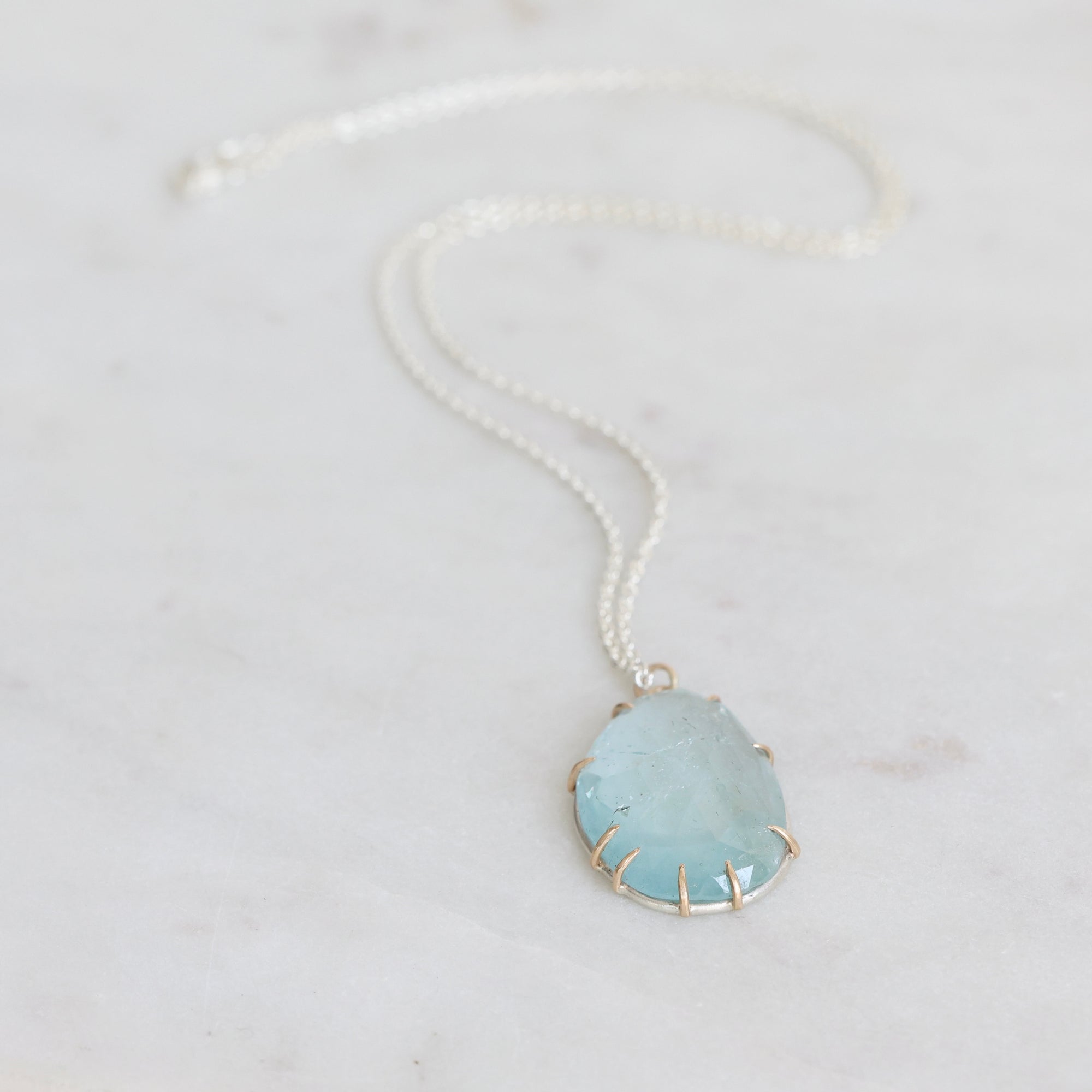 Necklace with a large teardrop-shaped green stone on a light gray background