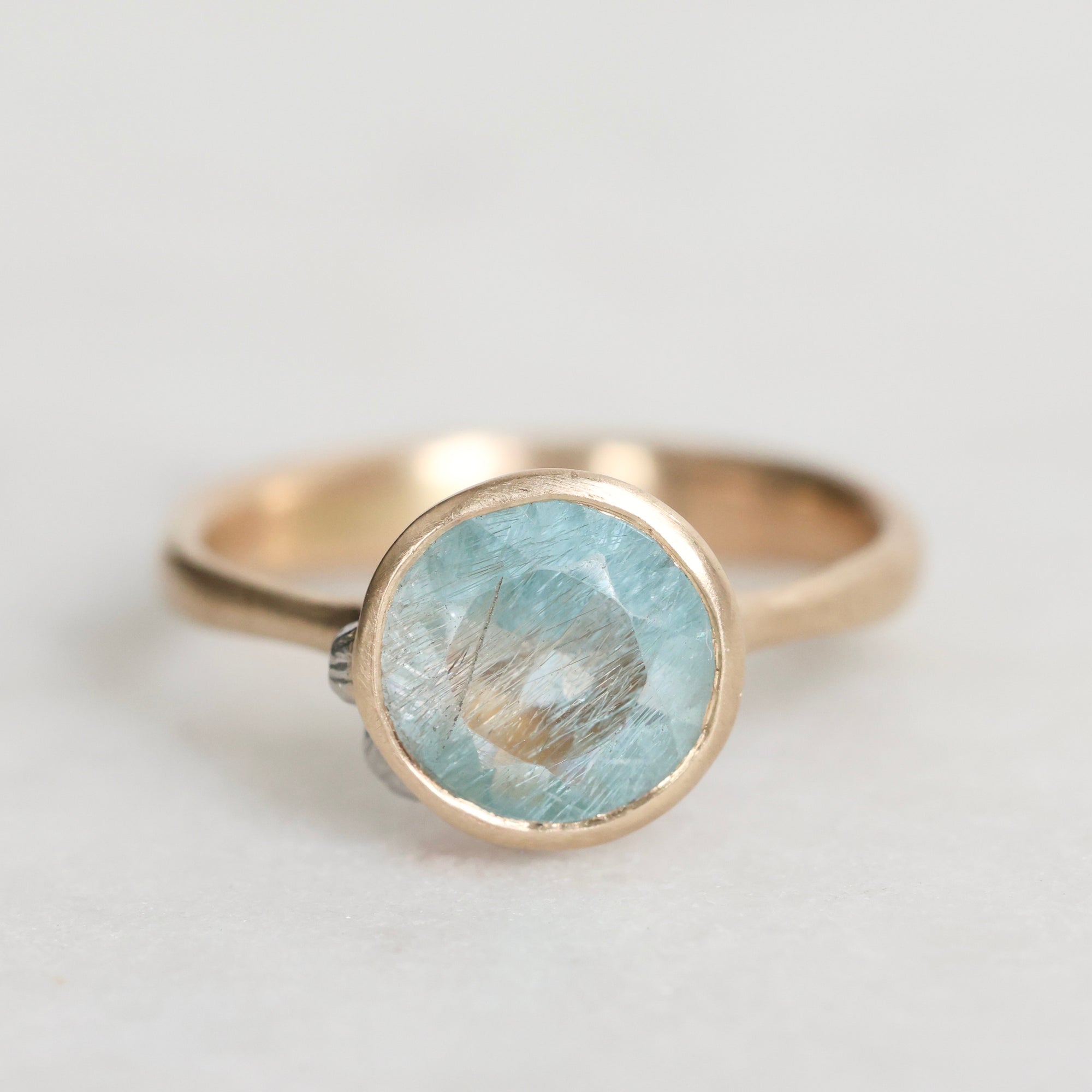 Gold ring with a light blue gemstone on a light gray background