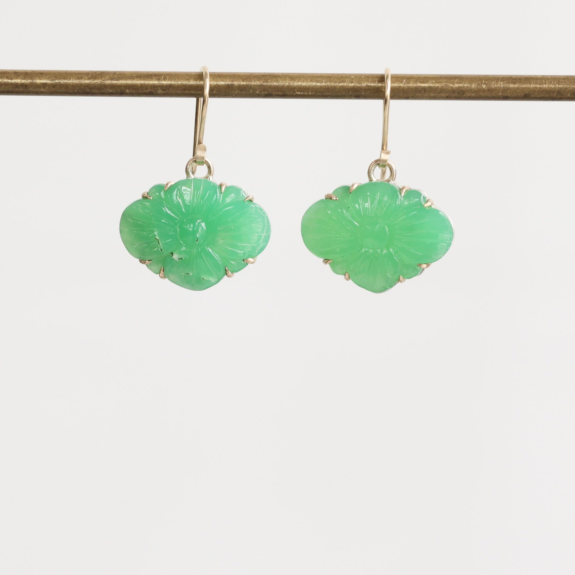 Pair of green earrings on a thin rod against a light gray background