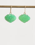Pair of green earrings on a thin rod against a light gray background