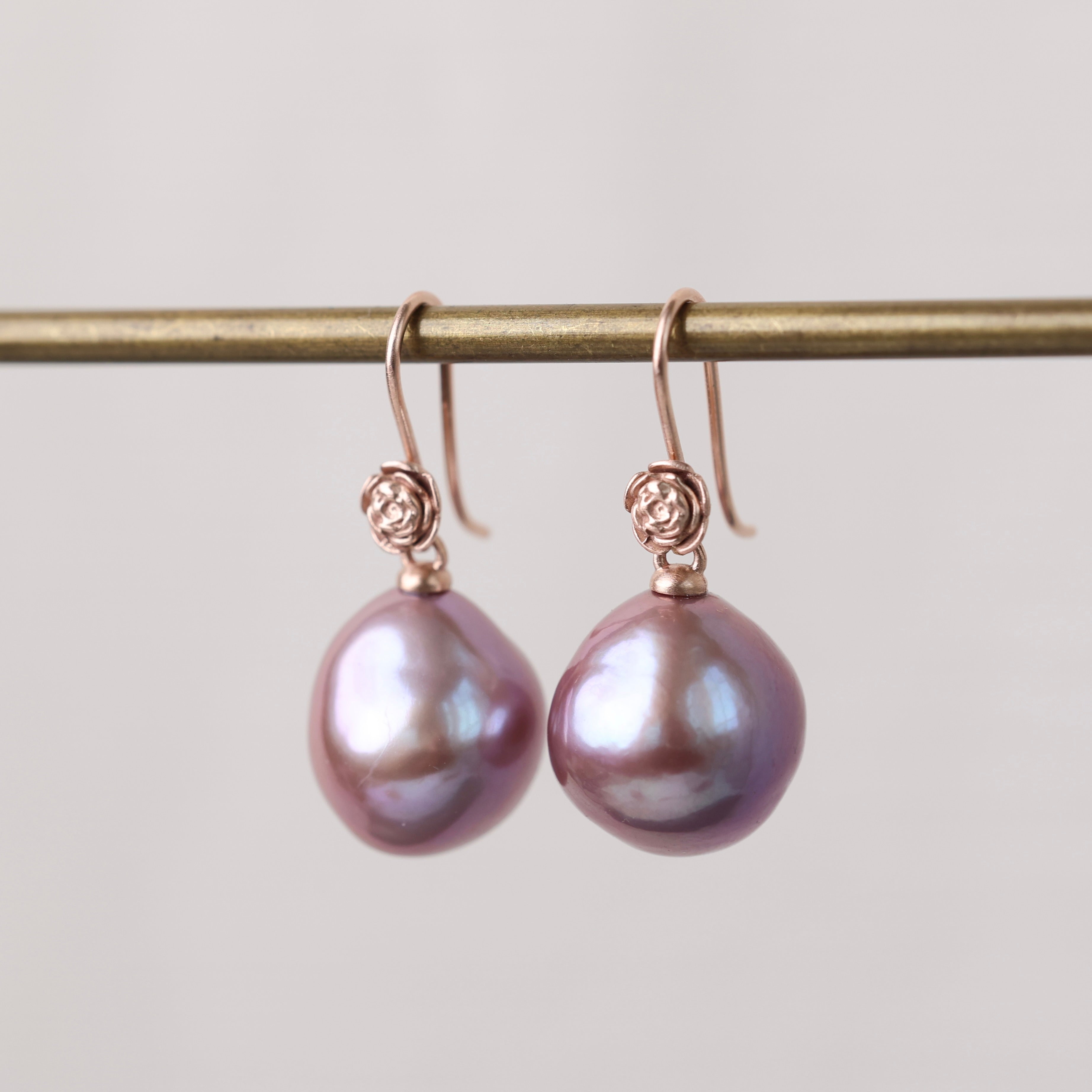 Pair of pink pearl earrings on a gold rod against a light gray background