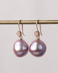 Pair of pink pearl earrings on a gold rod against a light gray background