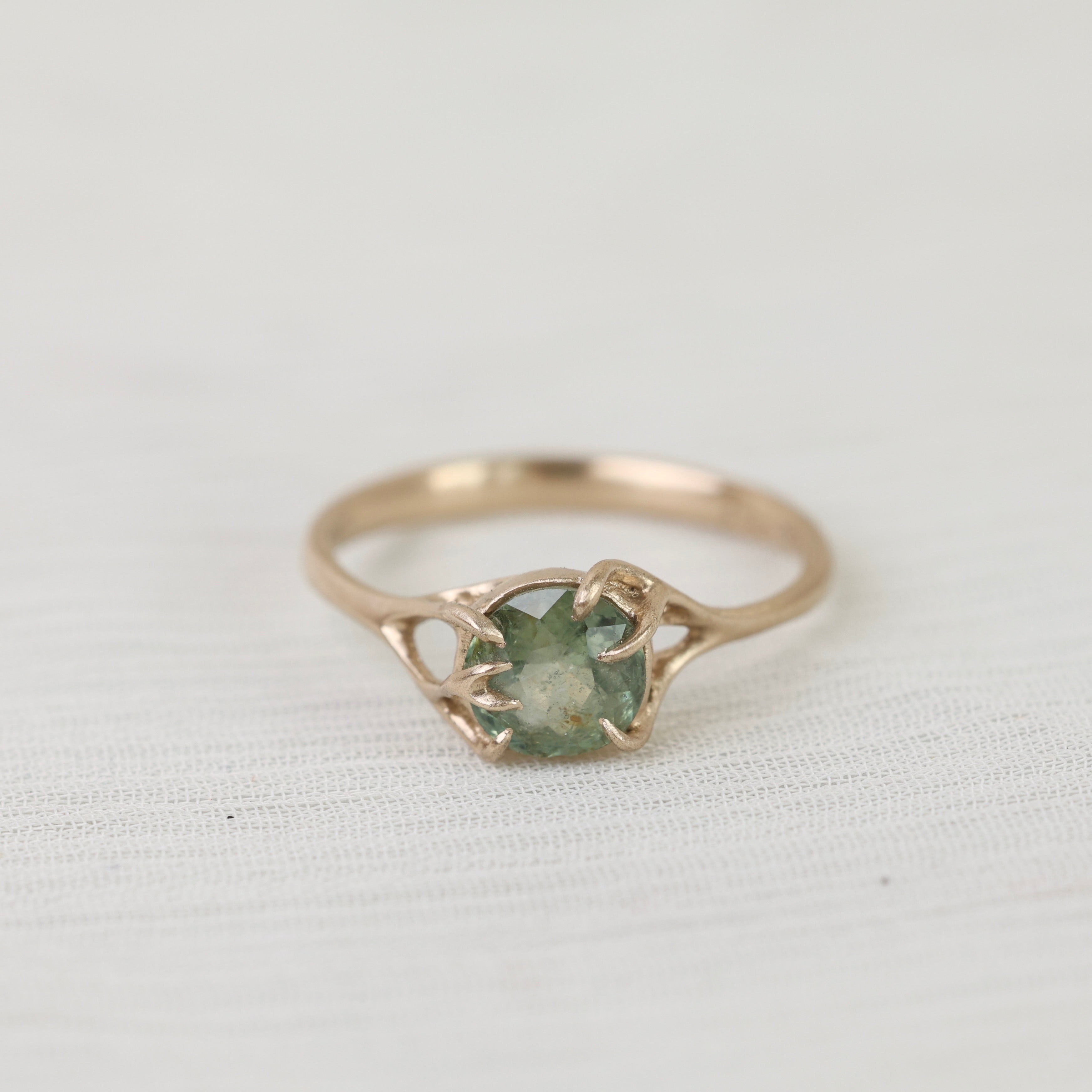 Gold ring with a green gemstone on a white fabric background