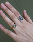 Hand wearing a gold ring with a blue gemstone on a neutral background
