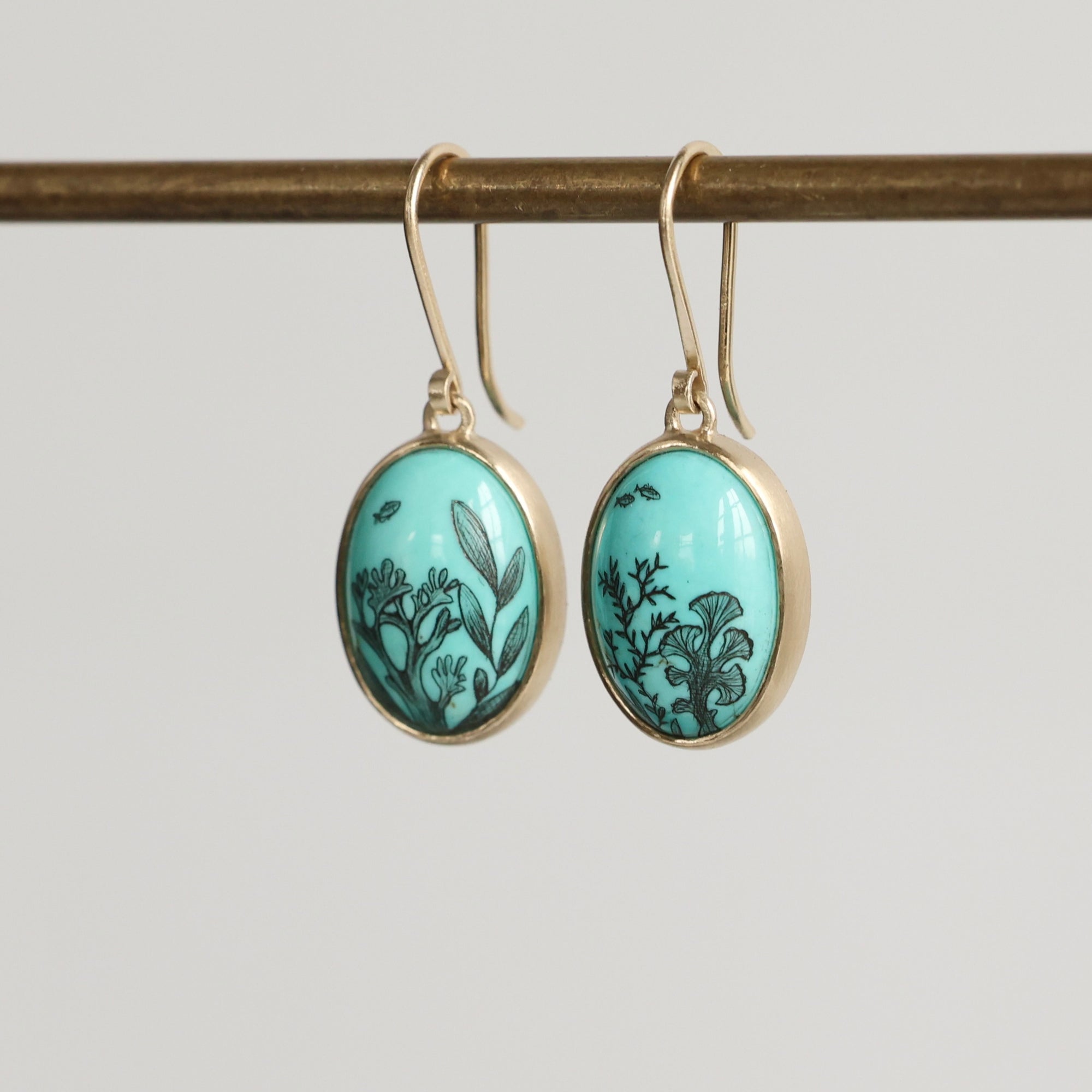 Pair of earrings with turquoise oval stones and gold accents on a gray background