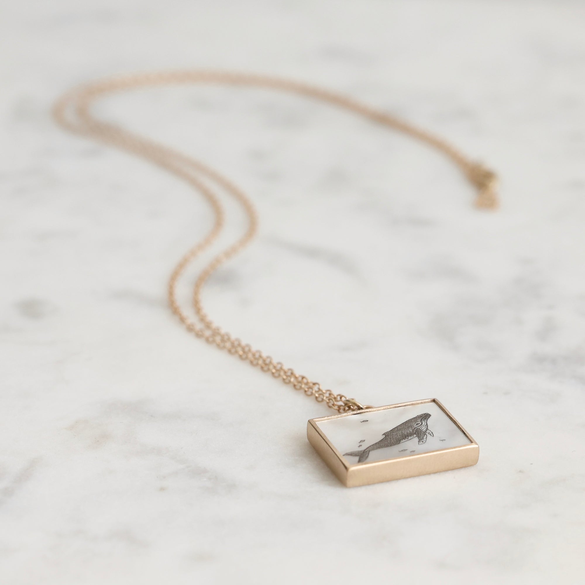 Gold necklace with a rectangular pendant on a marble surface