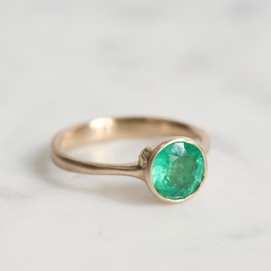 Gold ring with a green gemstone on a light gray background