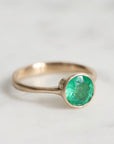 Gold ring with a green gemstone on a light gray background