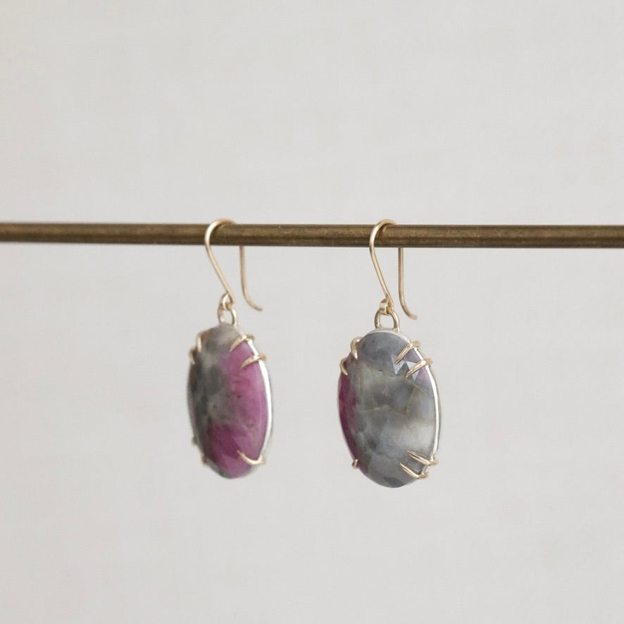 Pair of earrings with purple gemstones on a thin rod against a light gray background