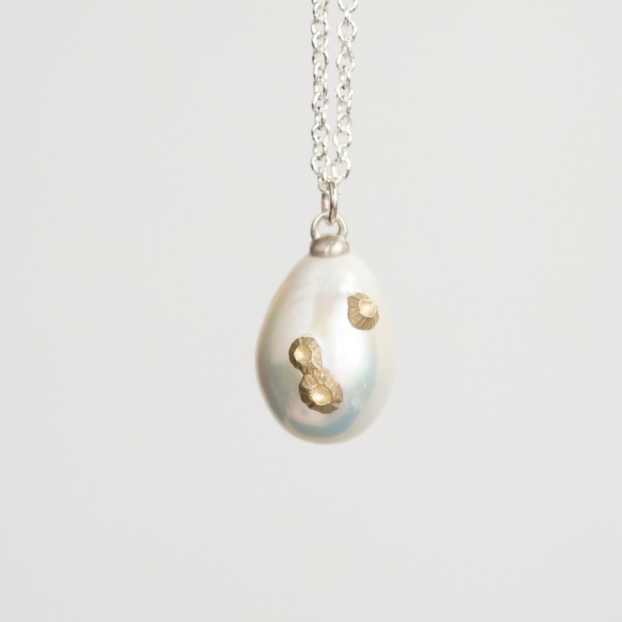Pearl pendant with gold accents on a silver chain against a light gray background