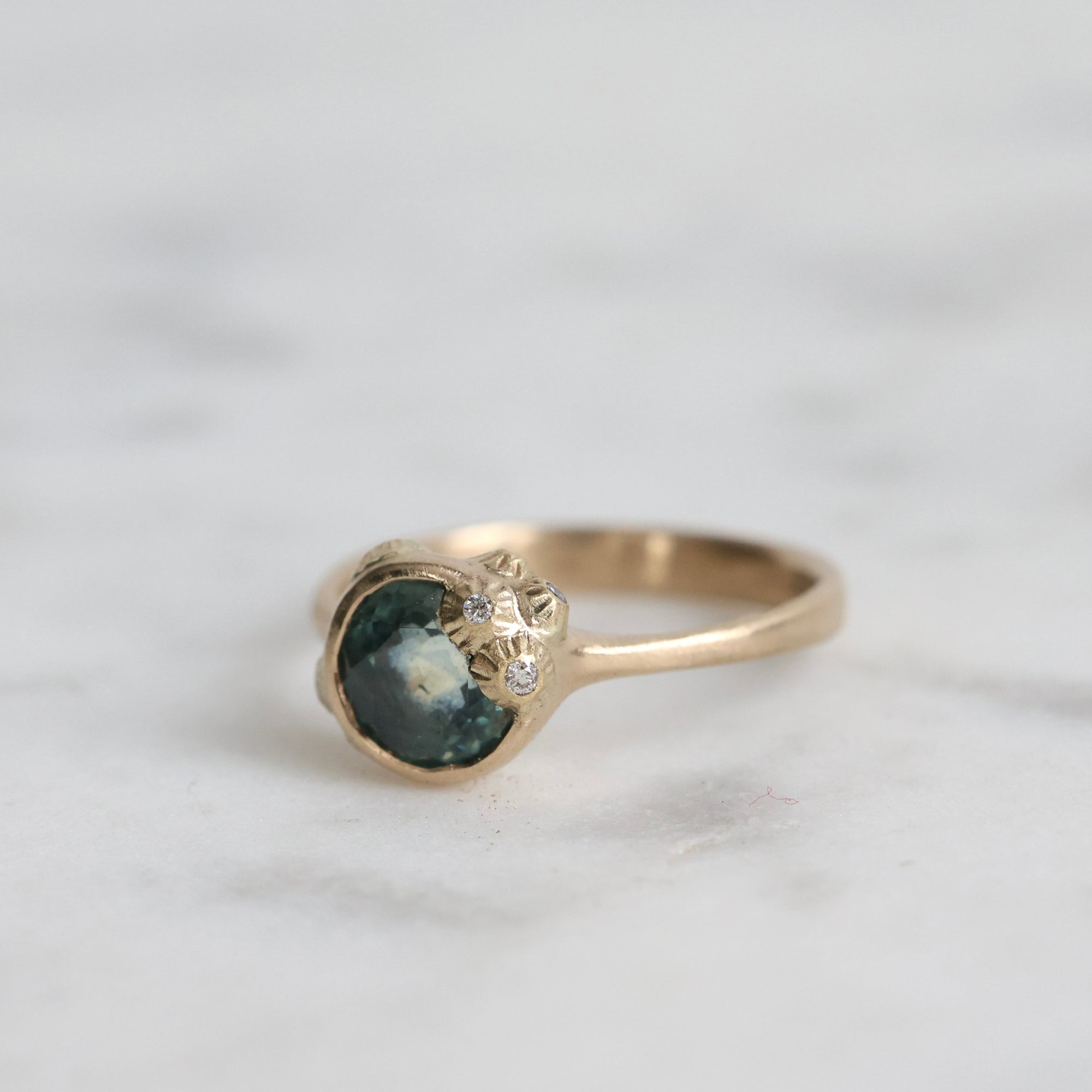 Gold ring with a green gemstone and diamond on a light gray background
