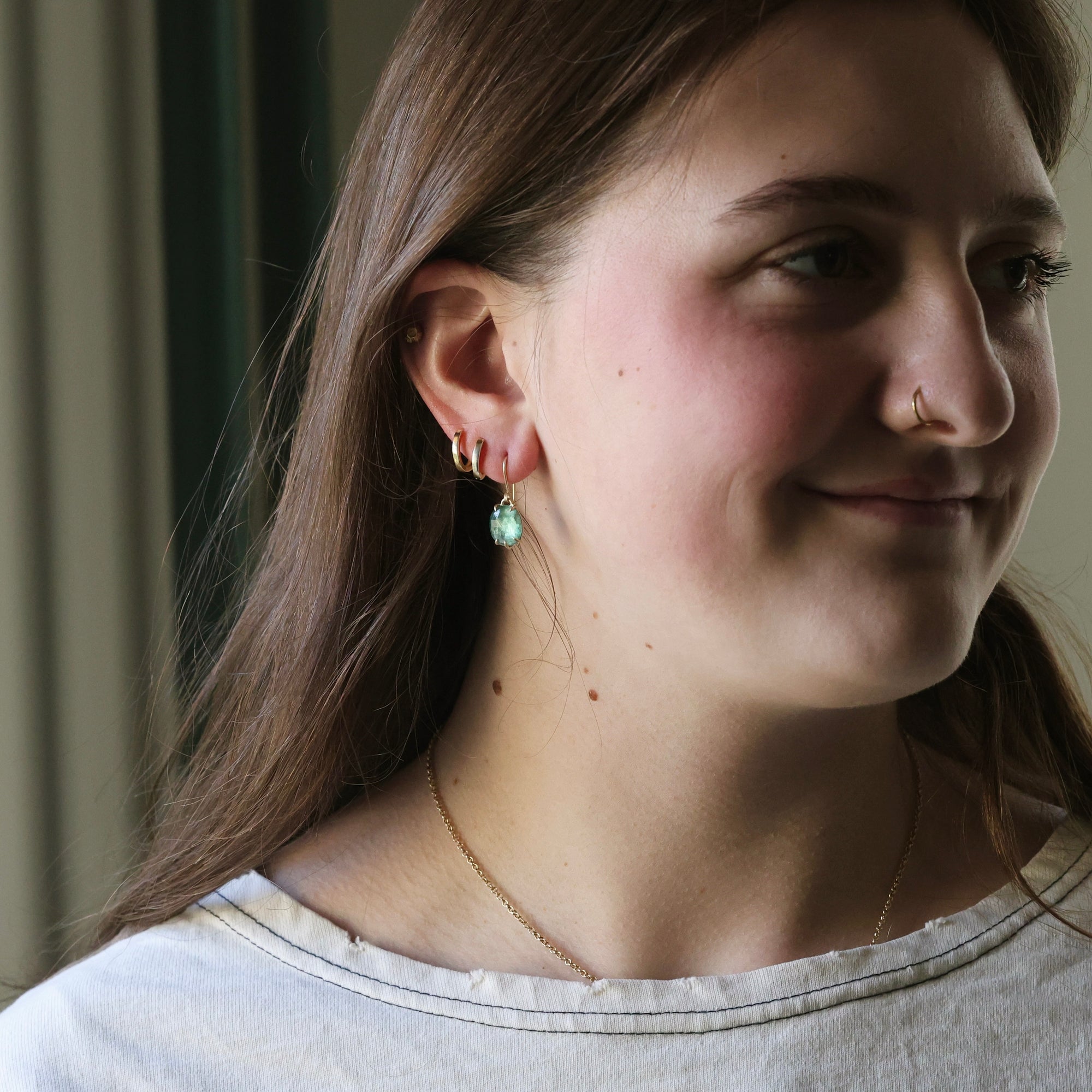 Close-up of a person wearing earrings and a nose ring, with a neutral background