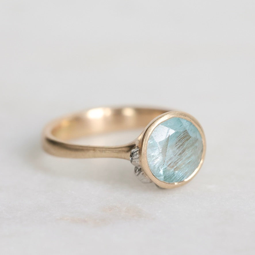 Gold ring with a light blue gemstone on a white background