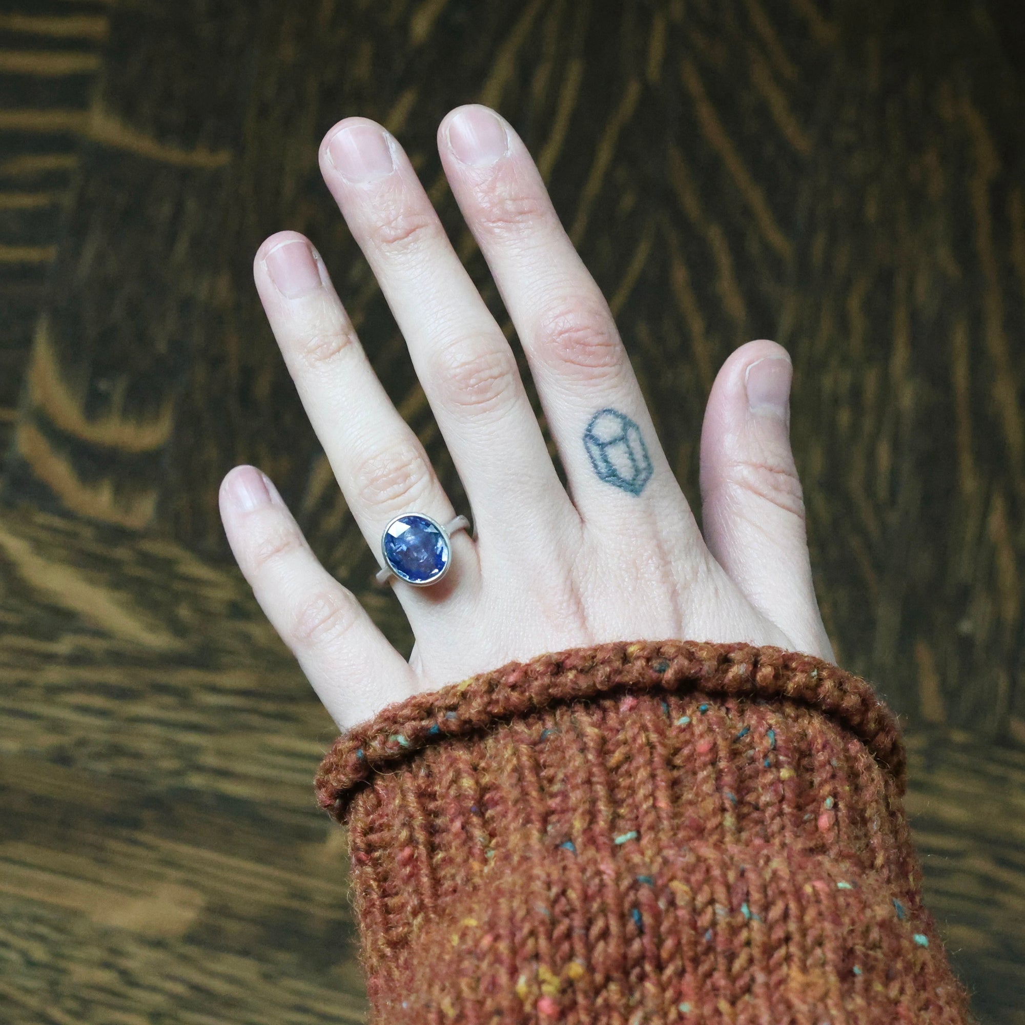 Hand wearing a ring with a blue gemstone against a textured brown background