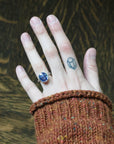 Hand wearing a ring with a blue gemstone against a textured brown background
