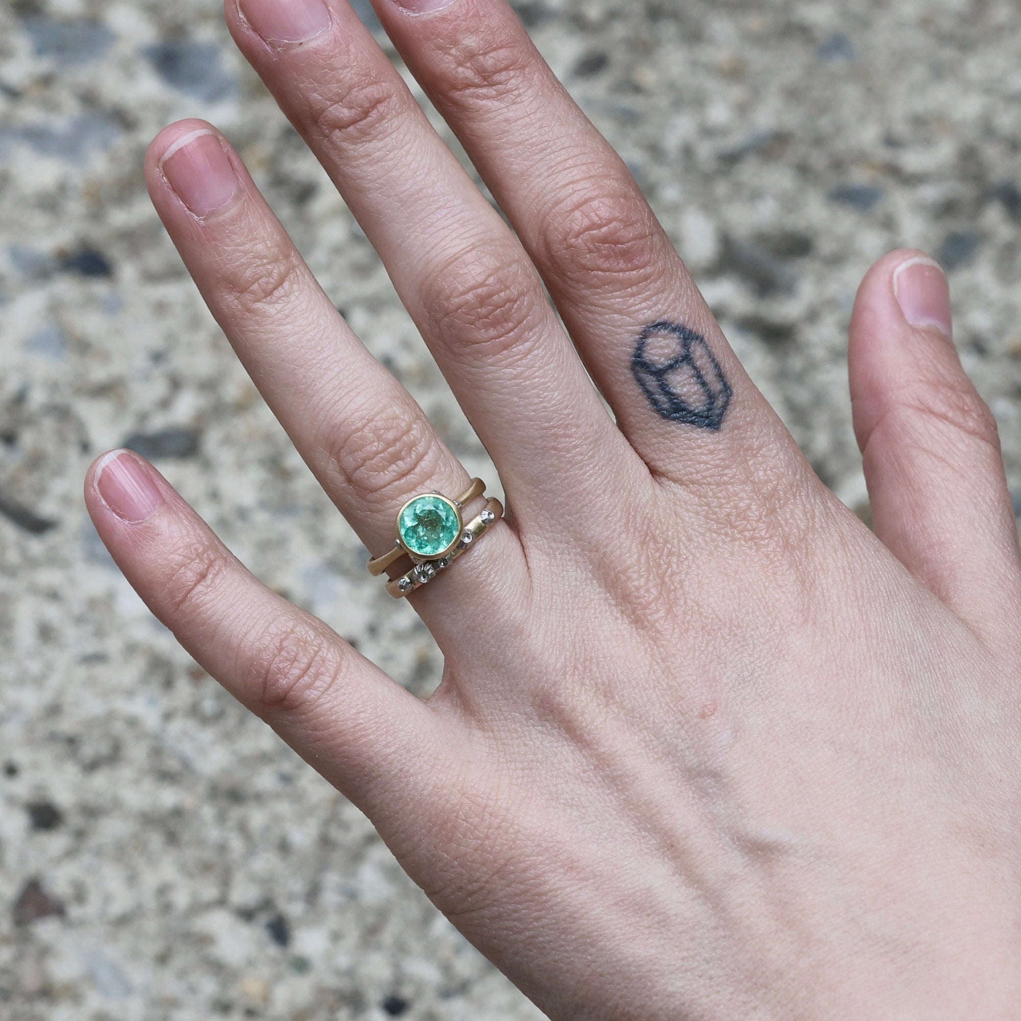 gold barnacle band on hand with green gemstone ring 