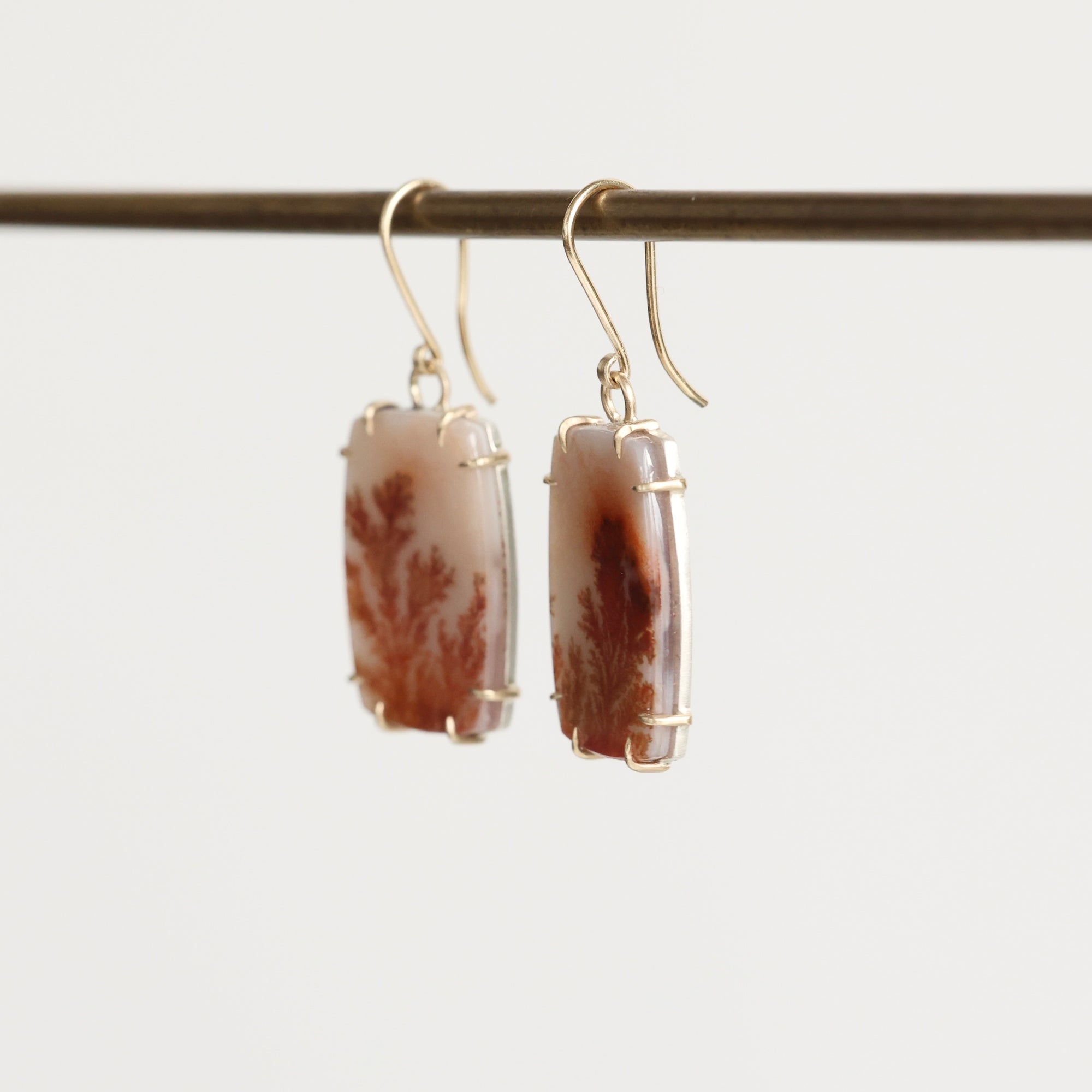 Pair of earrings with brown and white stone beads on a thin rod against a light background