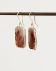 Pair of earrings with brown and white stone beads on a thin rod against a light background