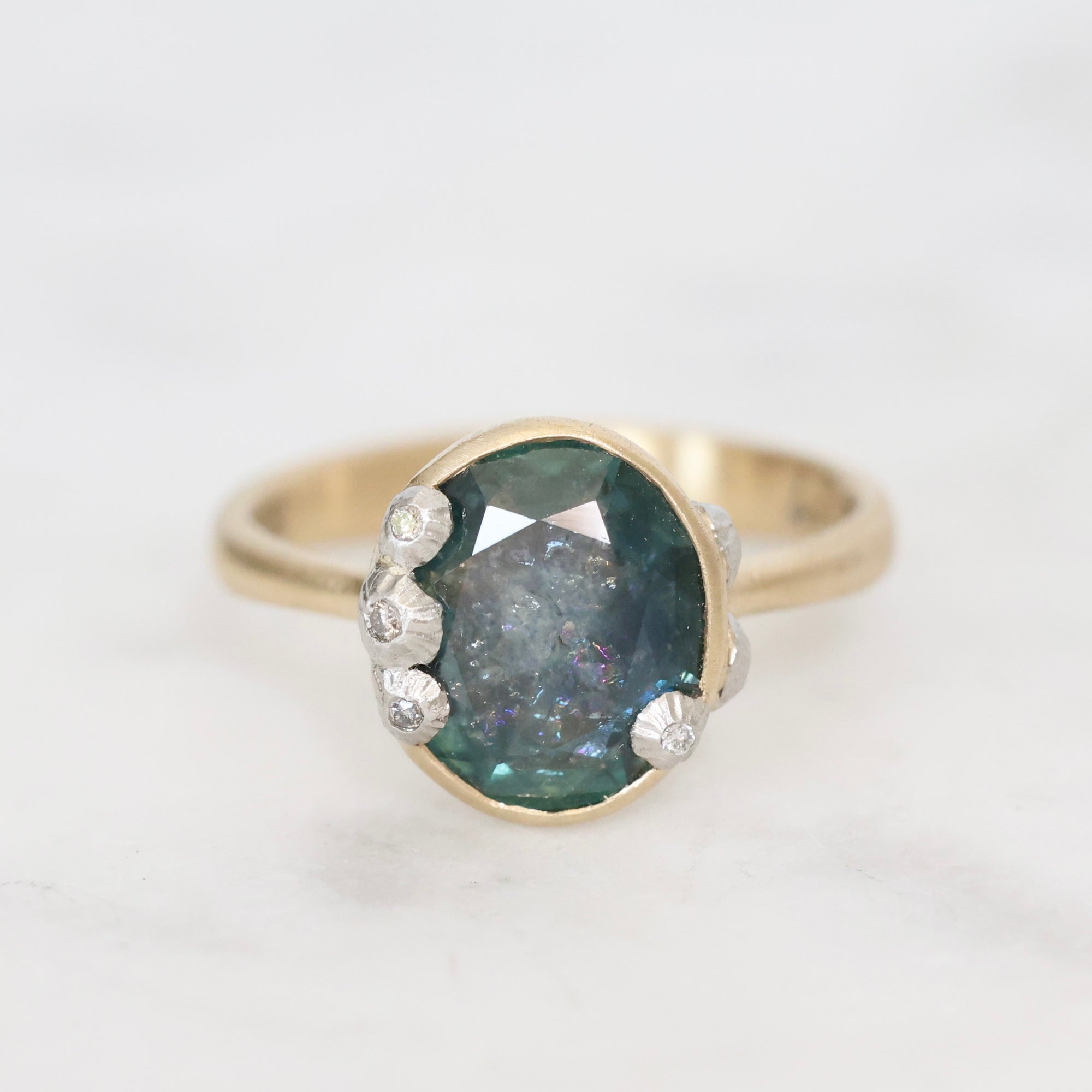 Gold ring with a large green gemstone and smaller diamonds on a white background