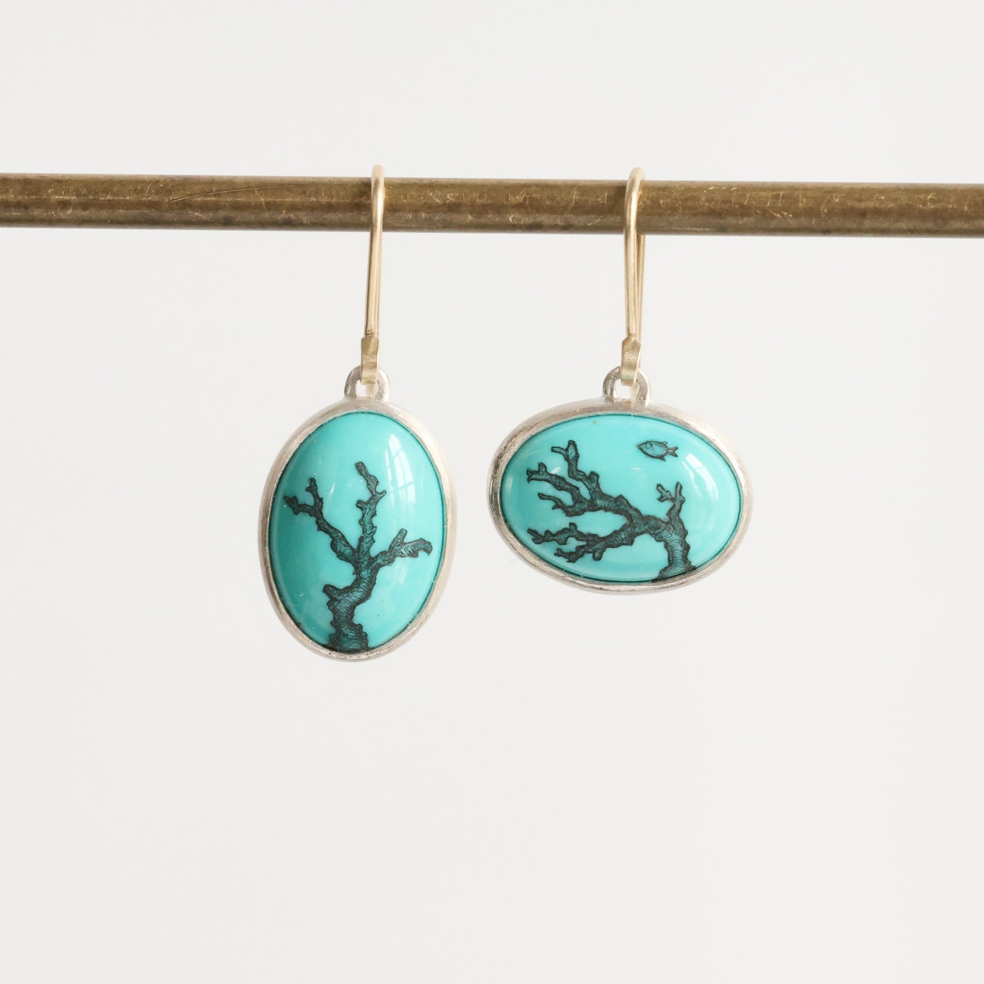 Pair of earrings with turquoise oval stones featuring black coral design on a white background.