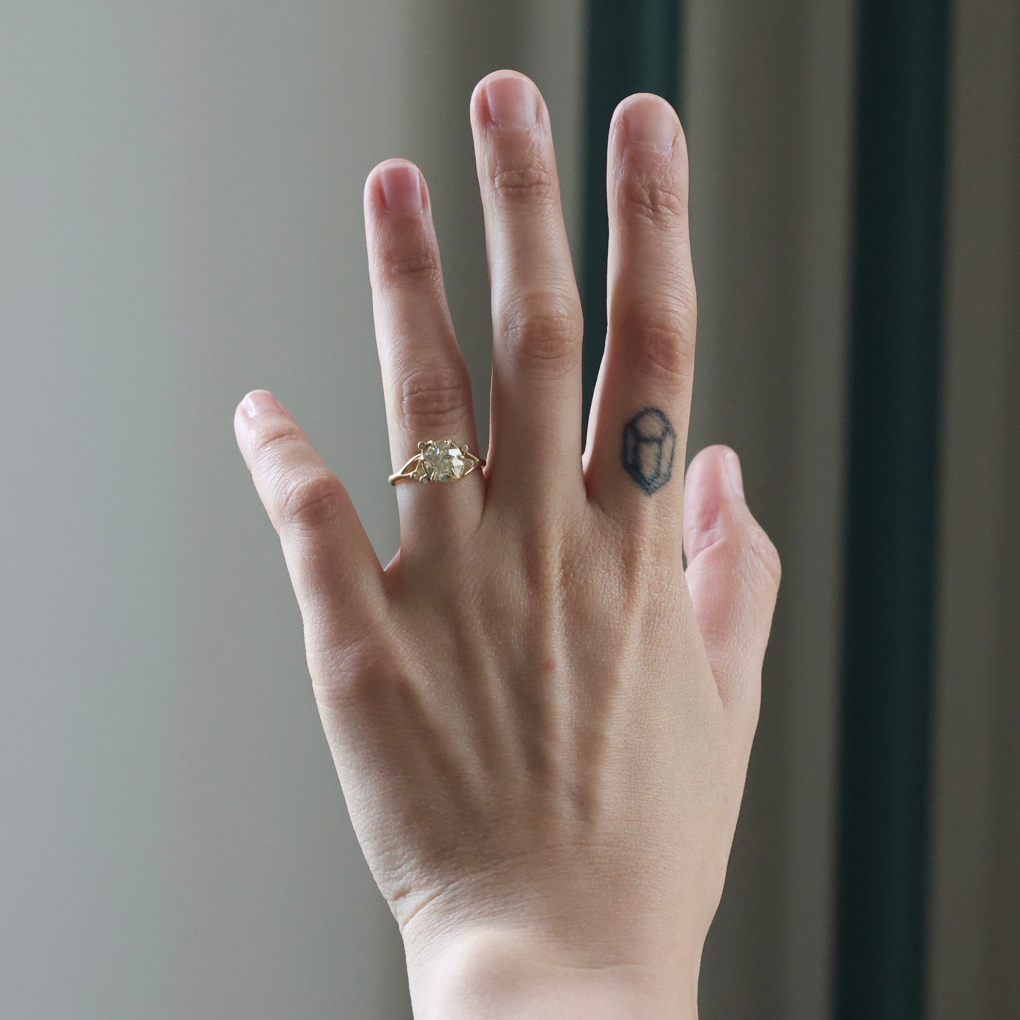 Hand wearing a gold ring with a diamond on a neutral background