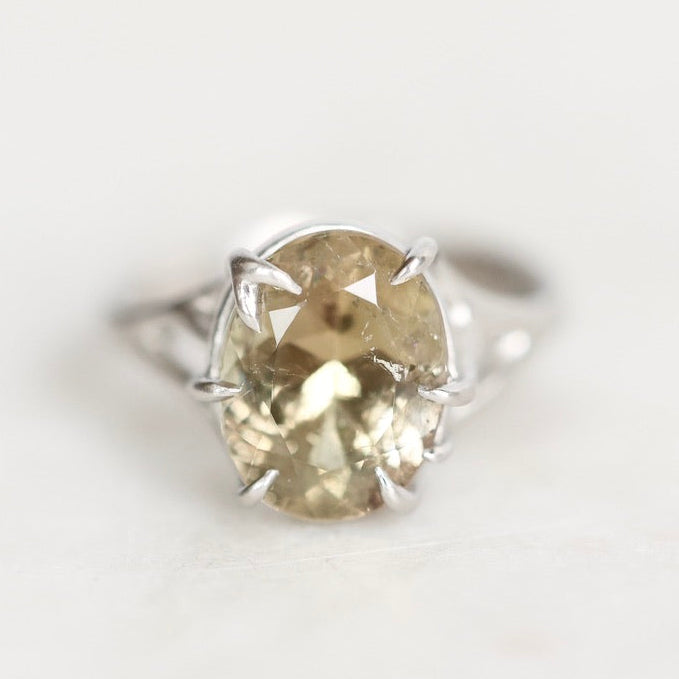 A silver ring featuring a large, oval-cut pale yellow gemstone in a prong setting, photographed on a clean white background.