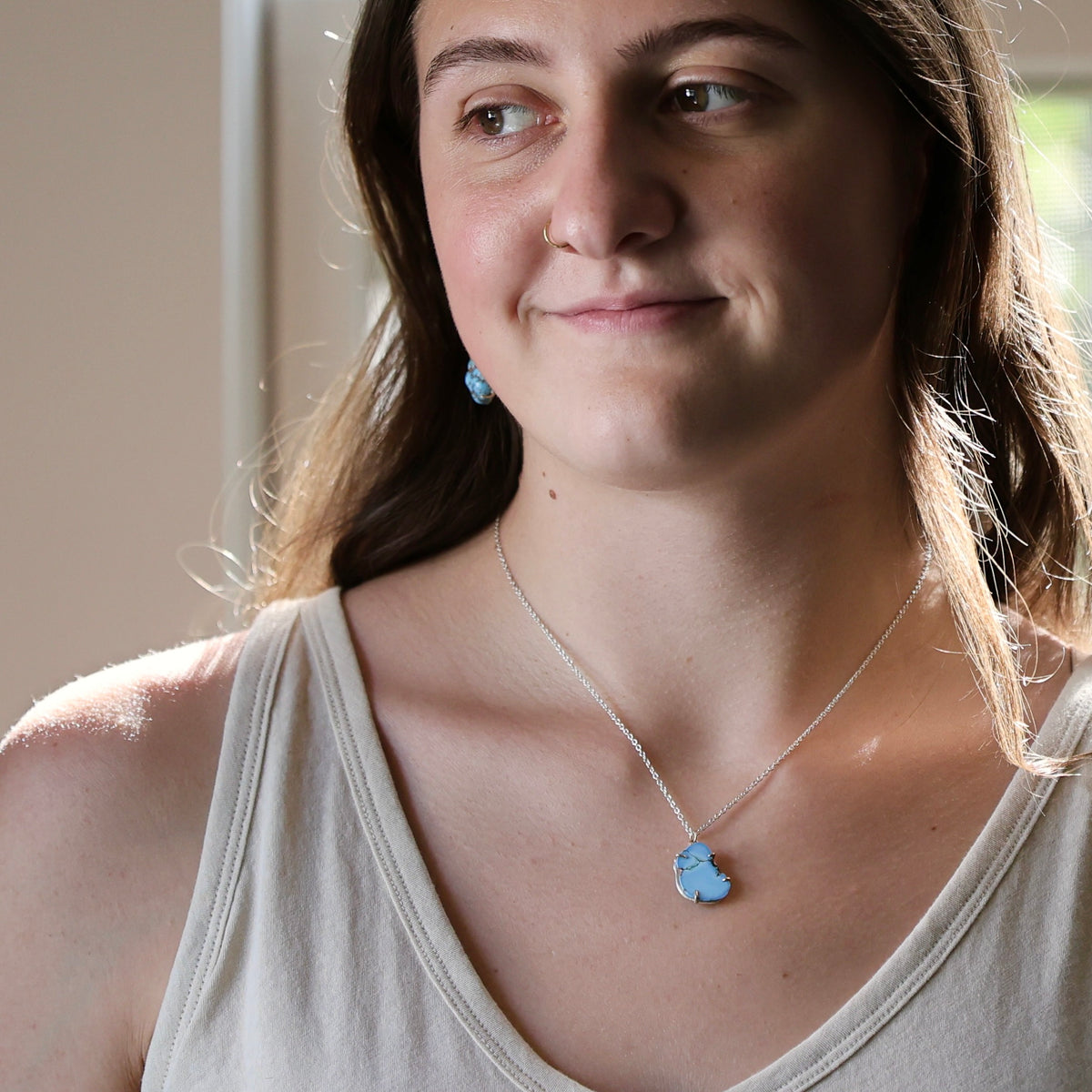 A woman wearing a silver chain necklace with a light blue elephant pendant, paired with a beige tank top.
