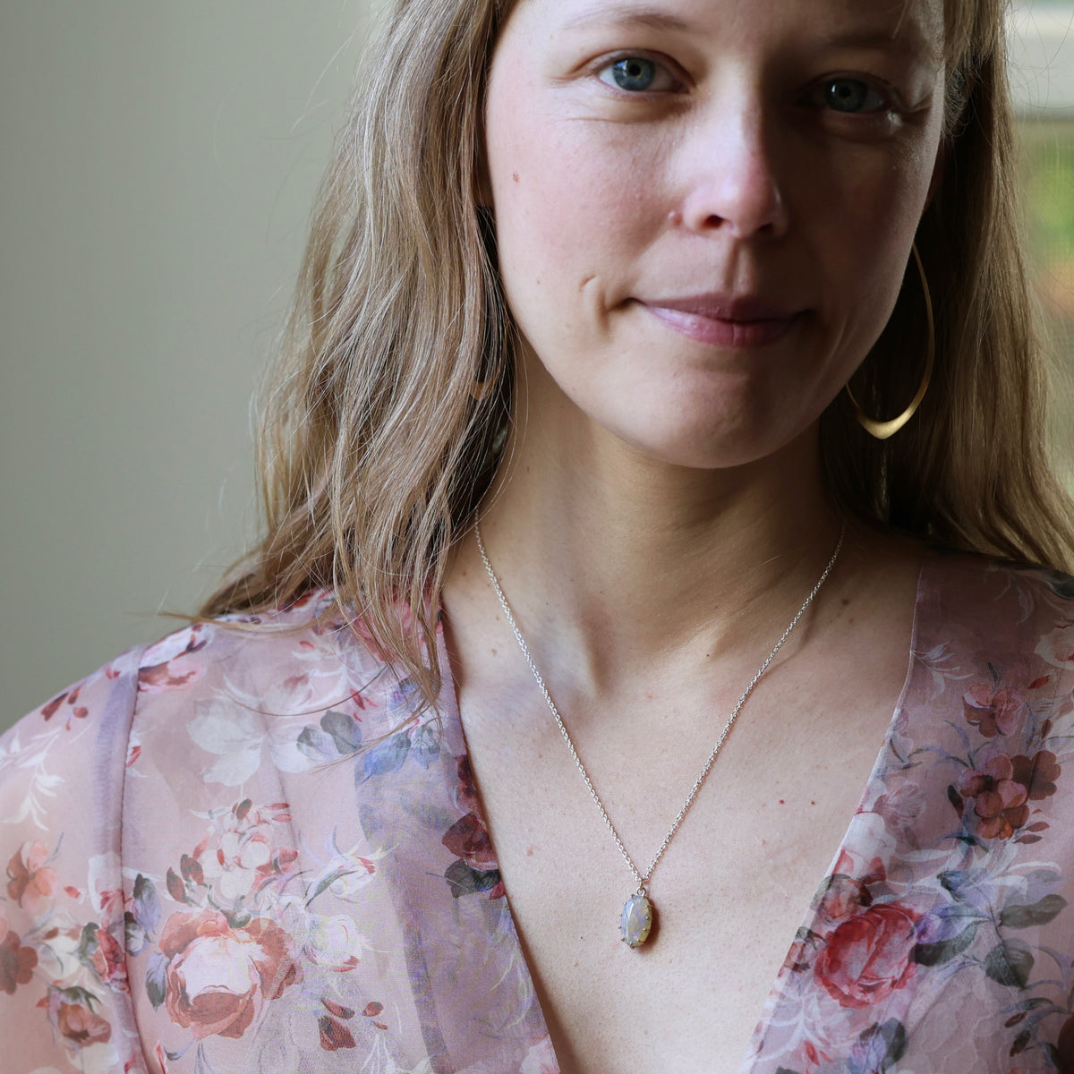Woman wearing opal necklace and floral blouse smiling at the camera against an indoor background. 