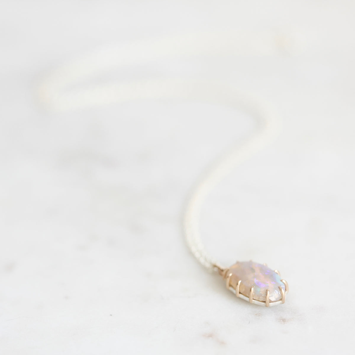 Opal necklace with silver chain and gold prongs laying on a marble background. 