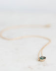 A delicate gold necklace with a small oval pendant featuring a dark green stone, resting on a light marble surface.