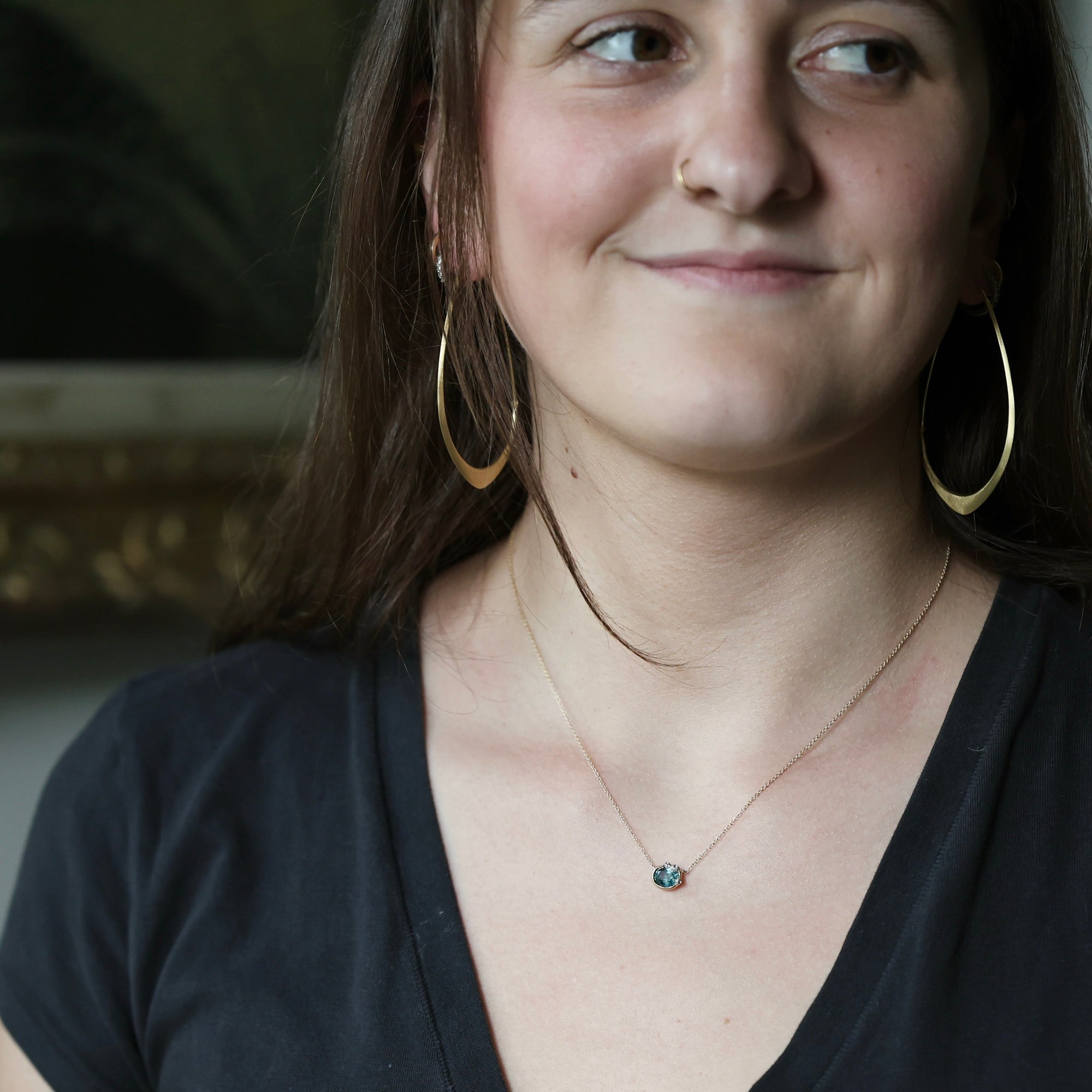 Woman wearing delicate green stone necklace and large hoop earrings