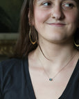 Woman wearing delicate green stone necklace and large hoop earrings