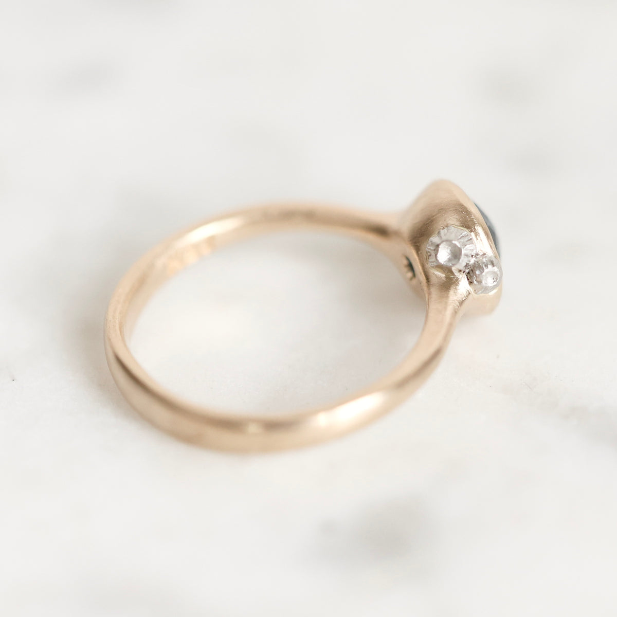 A close-up shot of a rose gold ring with a small clear gemstone, resting on a light marble surface.