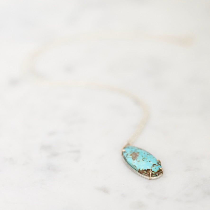 A silver necklace with an oval turquoise pendant resting on a light marble surface.