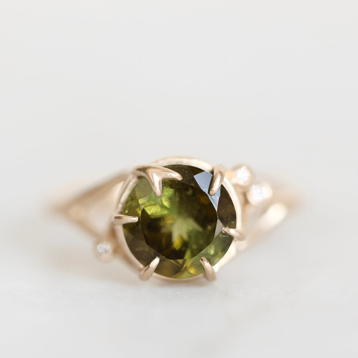 Green gemstone ring held in branchy gold prongs against a white background. 