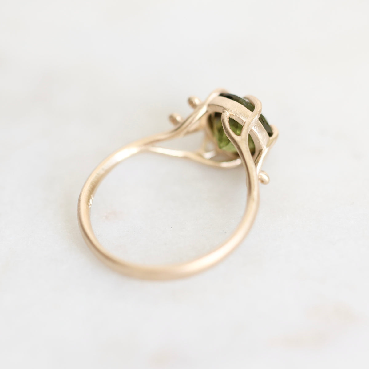 A gold ring with a small green gemstone, photographed on a light marble surface.