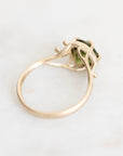 A gold ring with a small green gemstone, photographed on a light marble surface.