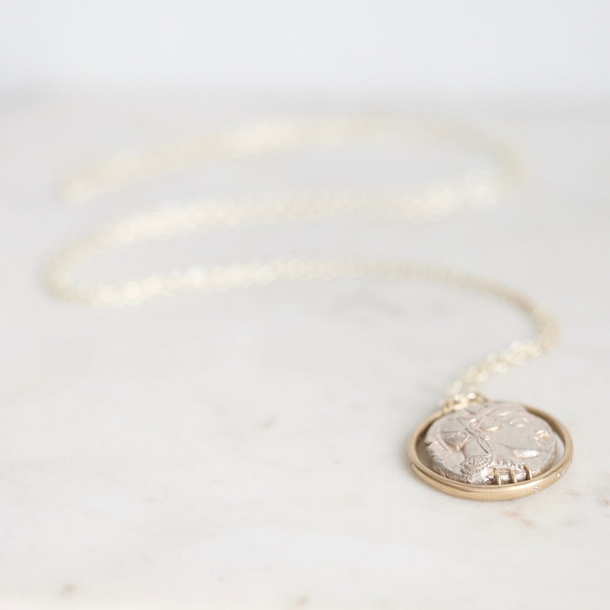 A silver-toned coin pendant necklace with a gold-toned bezel, resting on a light marble surface.