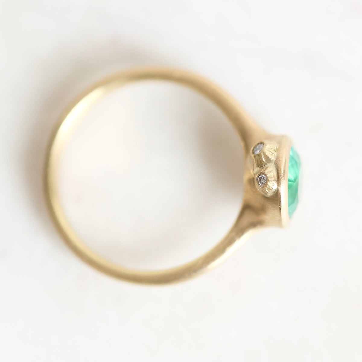 A gold ring with a green oval gemstone and small clear accent stones, photographed on a plain white background.