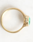 A gold ring with a green oval gemstone and small clear accent stones, photographed on a plain white background.