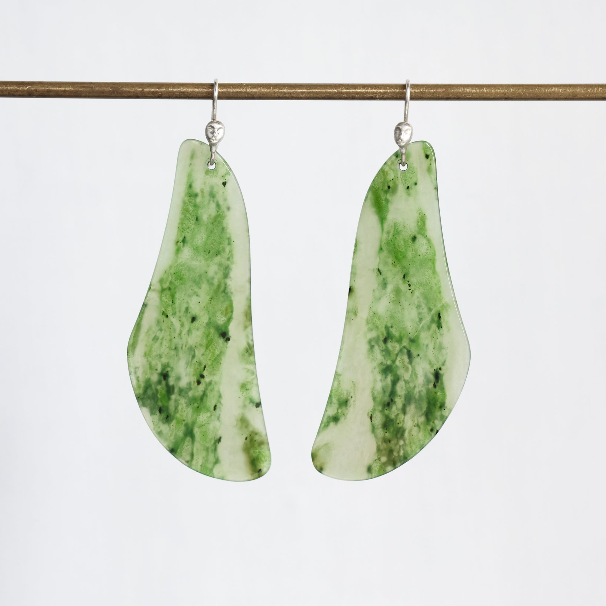 A pair of teardrop-shaped dangle earrings made from green and white marbled stone, hanging from silver fishhook wires against a plain white background.