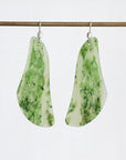 A pair of teardrop-shaped dangle earrings made from green and white marbled stone, hanging from silver fishhook wires against a plain white background.