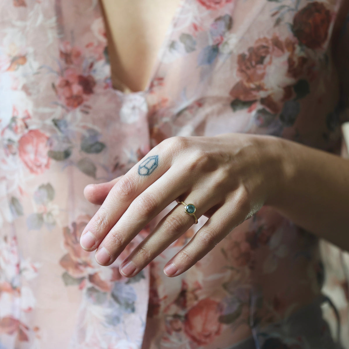 Hand wearing Ruthie B. bezel set ring in front of a floral blouse 