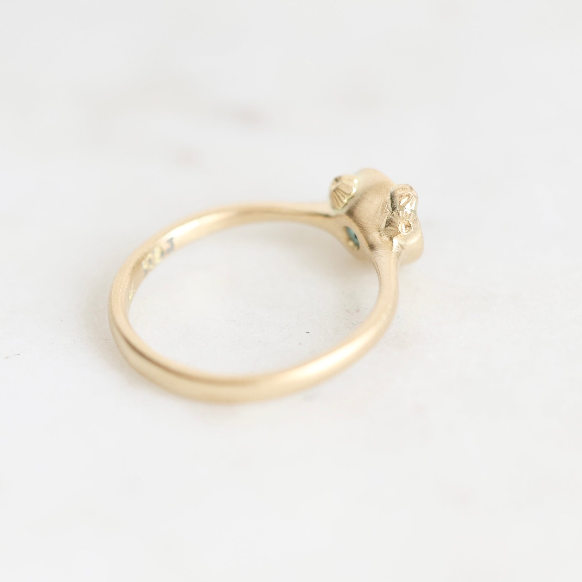 A delicate yellow gold ring photographed on a light, neutral background.