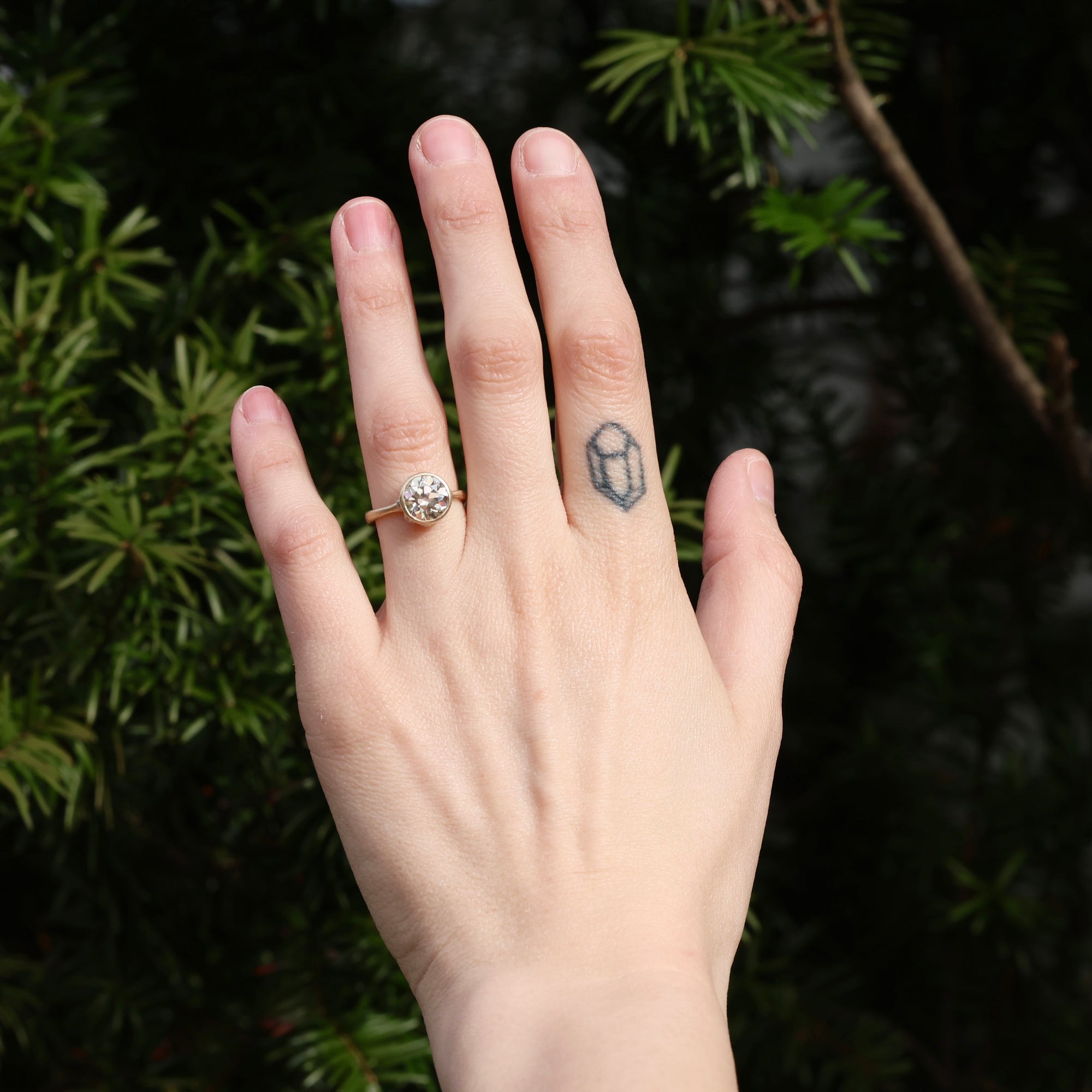 Hand wearing a ring with a geometric tattoo on the other finger against a dark background