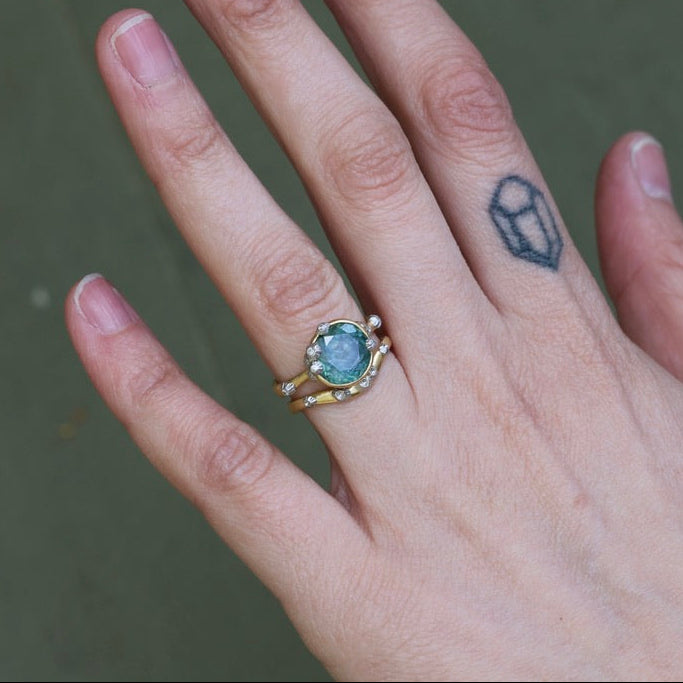 Hand wearing a ring with a green gemstone on a blurred background
