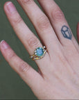 Hand wearing a ring with a green gemstone on a blurred background