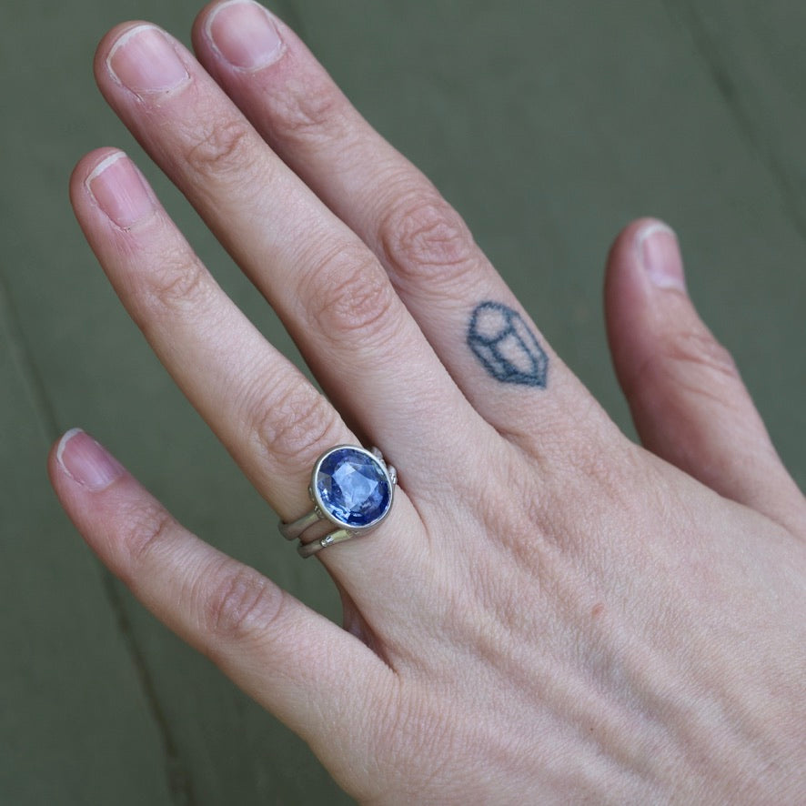 Hand wearing a ring with a blue gemstone on a neutral background