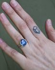 Hand wearing a ring with a blue gemstone on a neutral background